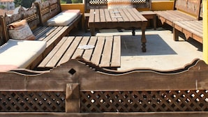 A rooftop terrace with wooden furniture and a view of a town and mountains.