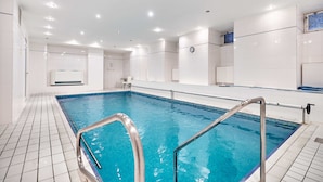 Une piscine intérieure moderne, avec une eau d’un bleu limpide, des murs carrelés et un escalier métallique.