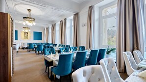 Une salle à manger élégante, avec une longue table, des chaises recouvertes d’un tissu bleu et un lustre.