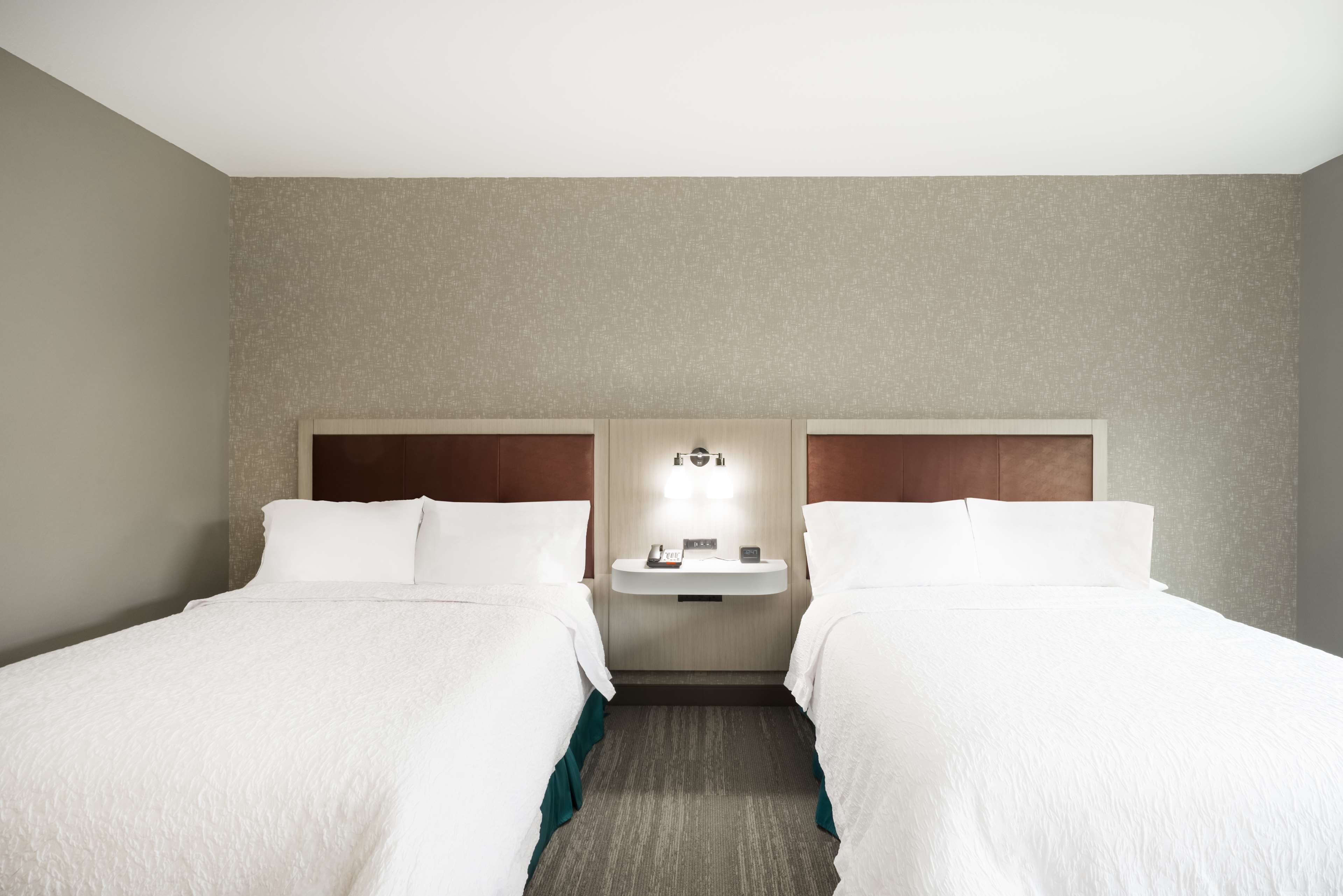 A hotel room with two beds, a small bedside table, and a wall-mounted light fixture.