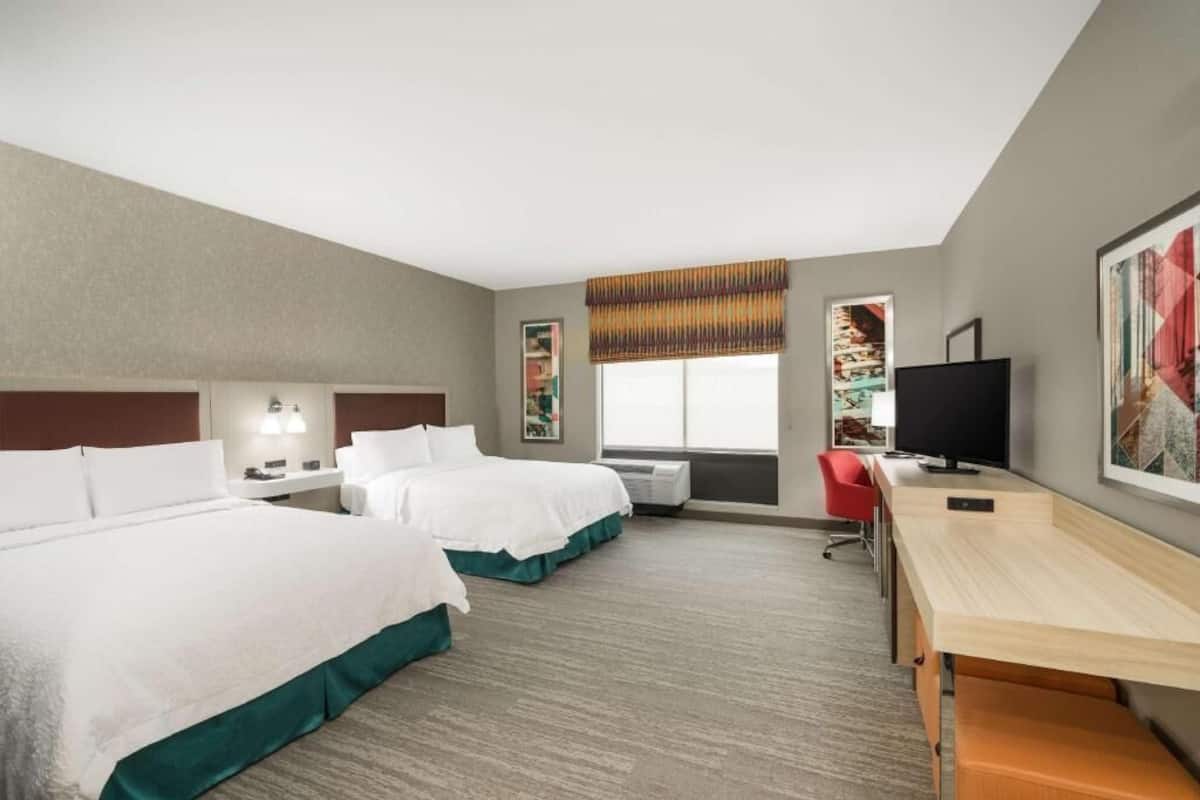 A hotel room with two beds, a desk, a TV, and a window with a view.