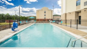 A swimming pool with lounge chairs and umbrellas, surrounded by a fence, and a building with a beige facade in the background. - Hampton Inn Newport (Newport)