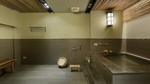 Ein modernes Badezimmer mit einer Holzbank, einem kleinen Hocker, einem Holzfass, einer Badewanne und einer Wandleuchte.