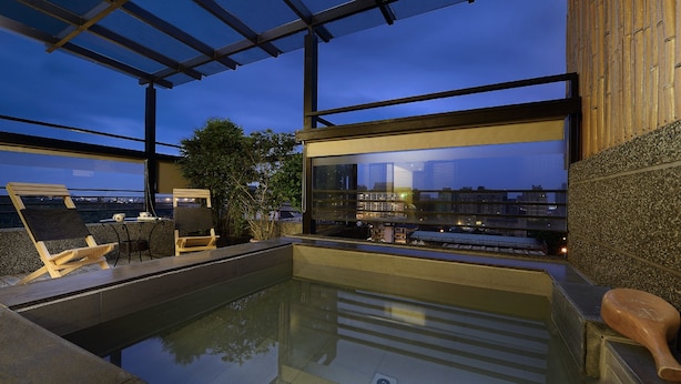 Ein Pool auf dem Dach mit Glaswänden, Holzliegen und Blick auf die Dämmerung über der Stadt.