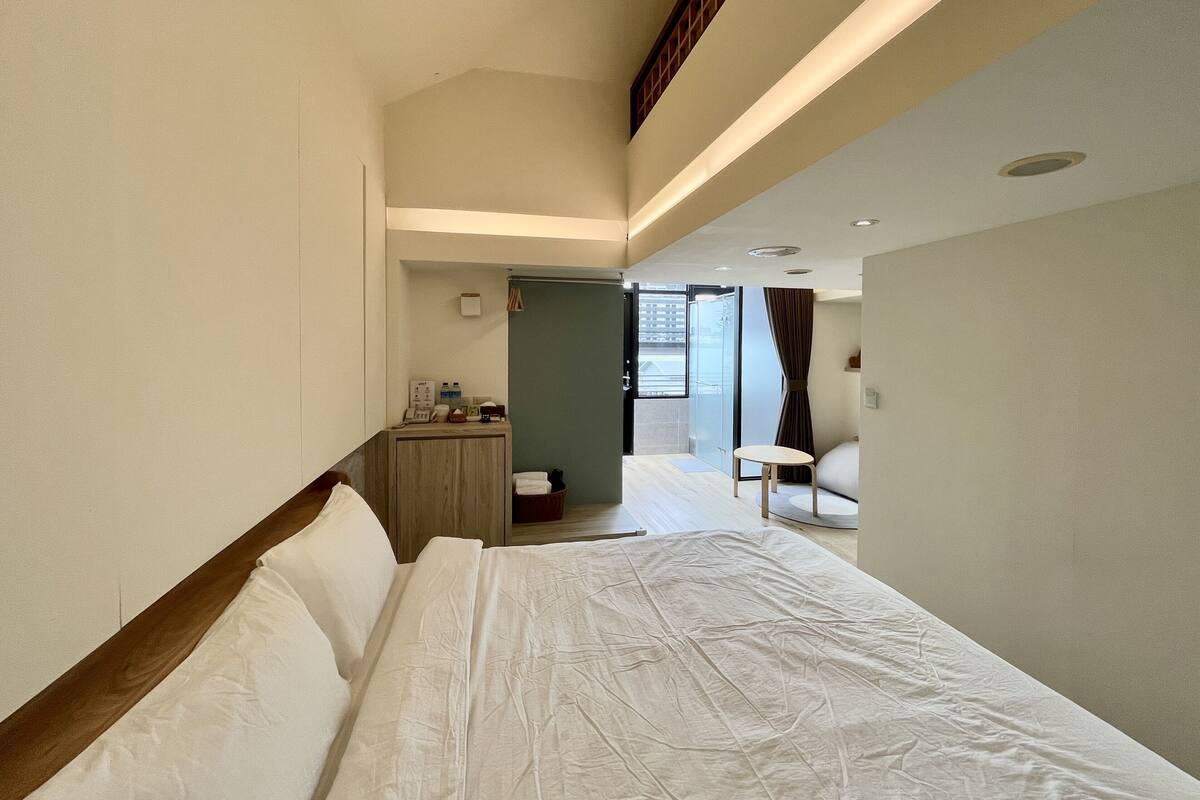 Hotelkamer met een groot bed, een bureau met stoel, een klein tafeltje en uitzicht buiten door een glazen deur.