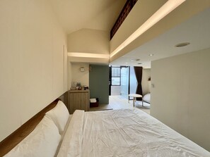 A hotel room with a large bed, a desk with a chair, a small table, and a view of the outside through a glass door. - Love Pine B&B (Jiaoxi)