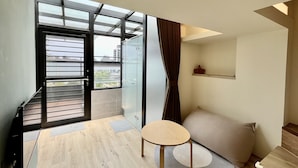 Ein modernes Zimmer mit Glastür zu einem Balkon, einem runden Tisch, einer Couch und einem kleinen Regal.