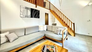 Un salon moderne avec un escalier en bois, un canapé d’angle et un magazine posé sur une table basse.