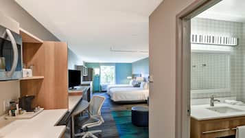 Une chambre d’hôtel équipée d’un bureau, d’une chaise, d’un lit et d’une salle de bain avec un lavabo et un miroir.