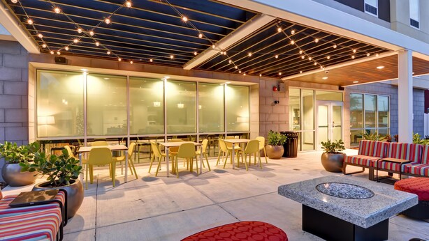 An outdoor seating area with tables and chairs, a fire pit, and potted plants. - Home2 Suites by Hilton Tampa USF Near Busch Gardens (Tampa)