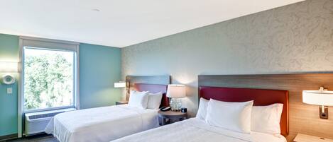 Hotellihuone, jossa on kaksi sänkyä, ikkuna, josta avautuu näkymä puihin, ja marmorikuvioitu seinä.