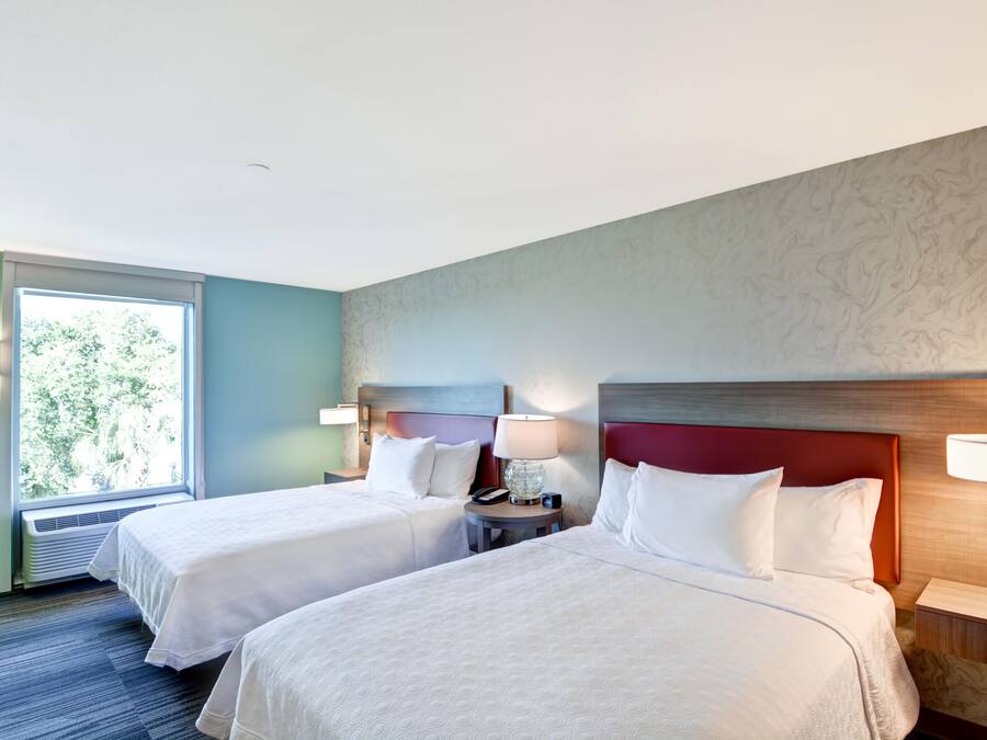 A hotel room with two beds, a window with a view of trees, and a marble-patterned wall.