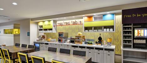Um restaurante moderno com uma mesa comunitária grande, área de cozinha e balcão com diversos alimentos.