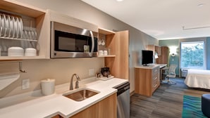 A modern kitchen with a microwave, sink, and coffee maker, a small TV, and a view of the outdoors. - Home2 Suites by Hilton Tampa USF Near Busch Gardens (Tampa)