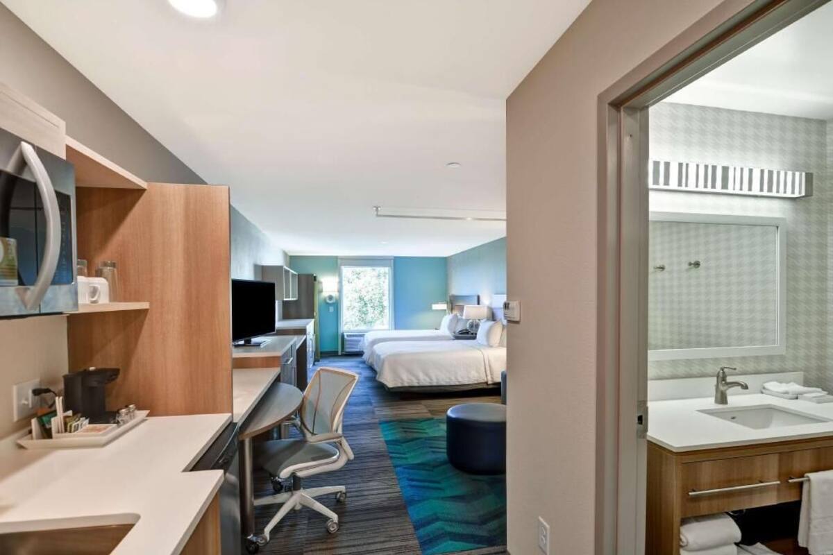 Una habitación de hotel con escritorio, silla, cama y baño con lavamanos y espejo.