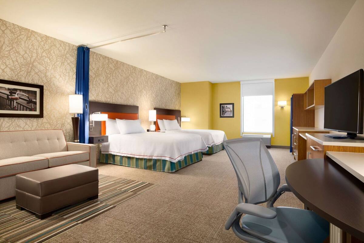 A hotel room with two beds, a sofa, a desk, and a television.