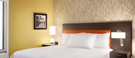 A hotel room with a large bed, a nightstand with a lamp, a wall-mounted light, and a framed picture on the wall.
