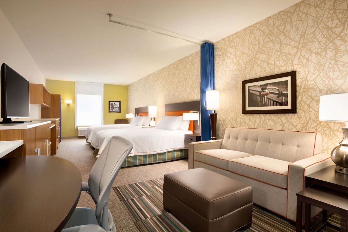 A hotel room with a bed, a sofa, a desk, a chair, and a television.