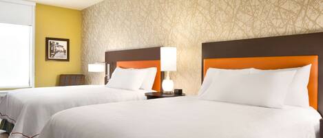 A hotel room with two beds, each with white bedding and orange headboards. There is a framed picture on the wall and a lamp on the nightstand.