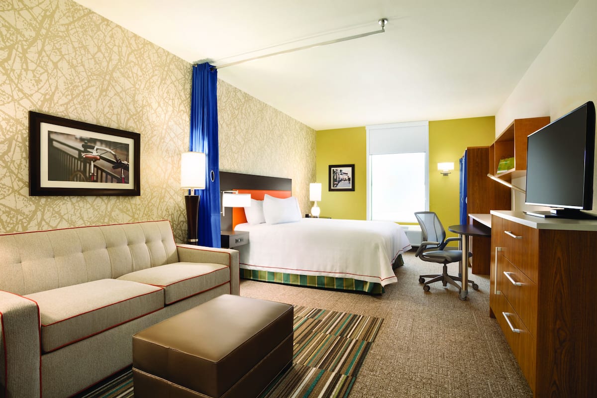 A hotel room with a bed, a sofa, a TV, a desk, and a chair.