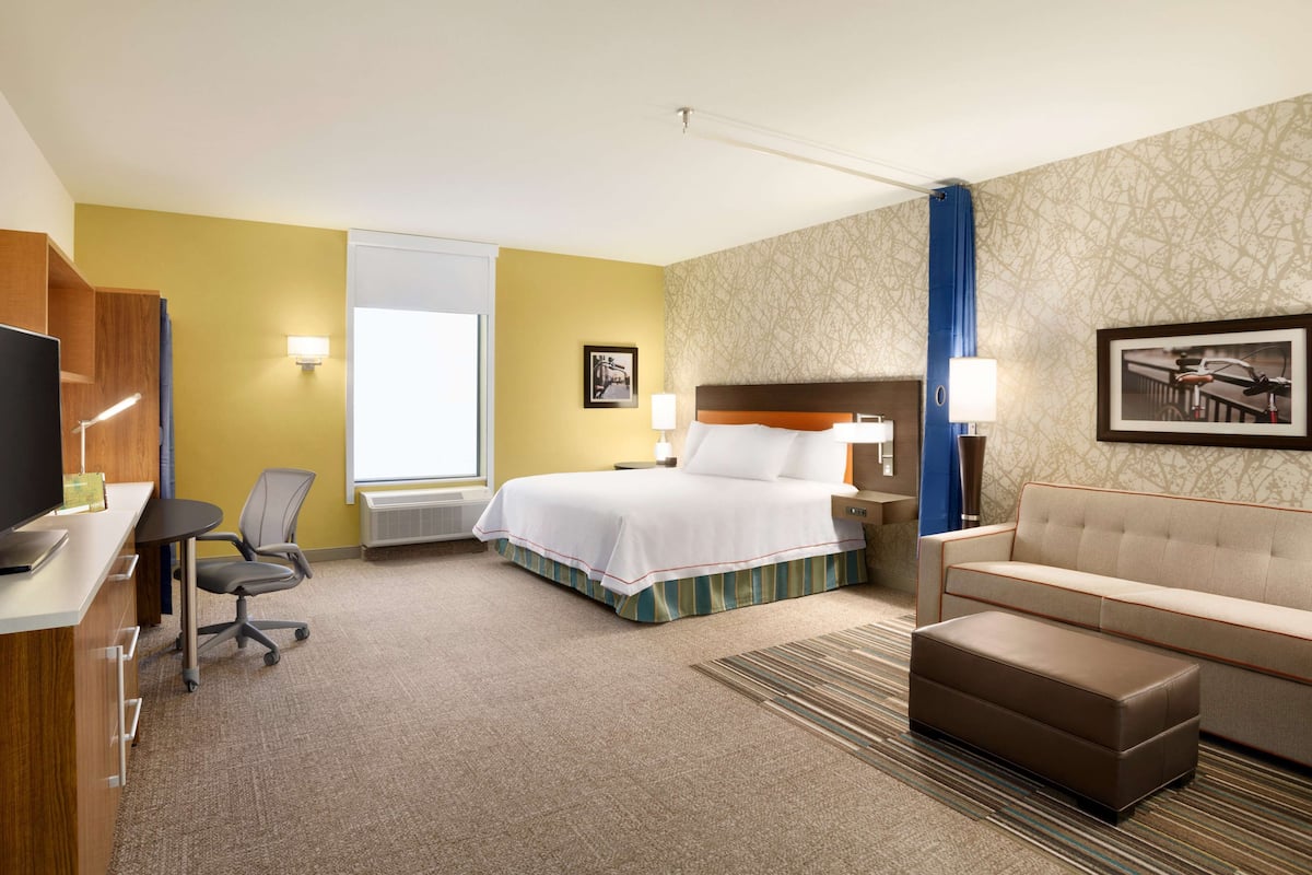A hotel room with a bed, a desk with a computer, a chair, a sofa, and a television.