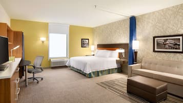 A hotel room with a bed, a desk with a computer, a chair, a sofa, and a television.