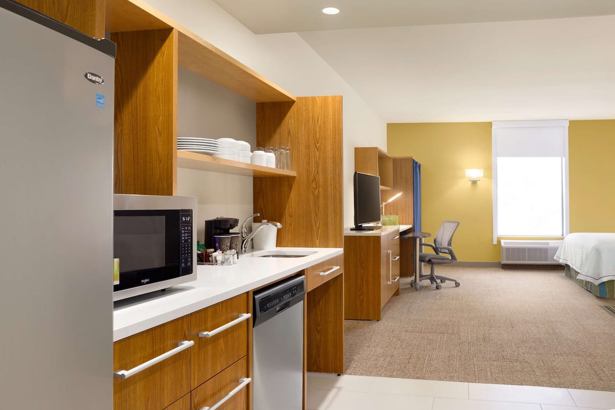 A modern kitchen with a refrigerator, microwave, and dishwasher, wooden cabinets, and a small dining area with a table and chairs.