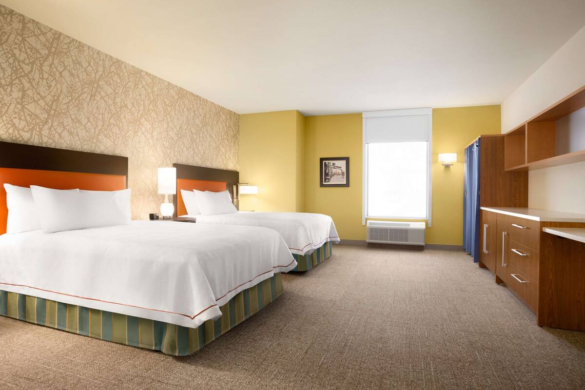 A hotel room with two beds, a large window, a wardrobe, and a wall with a patterned design.