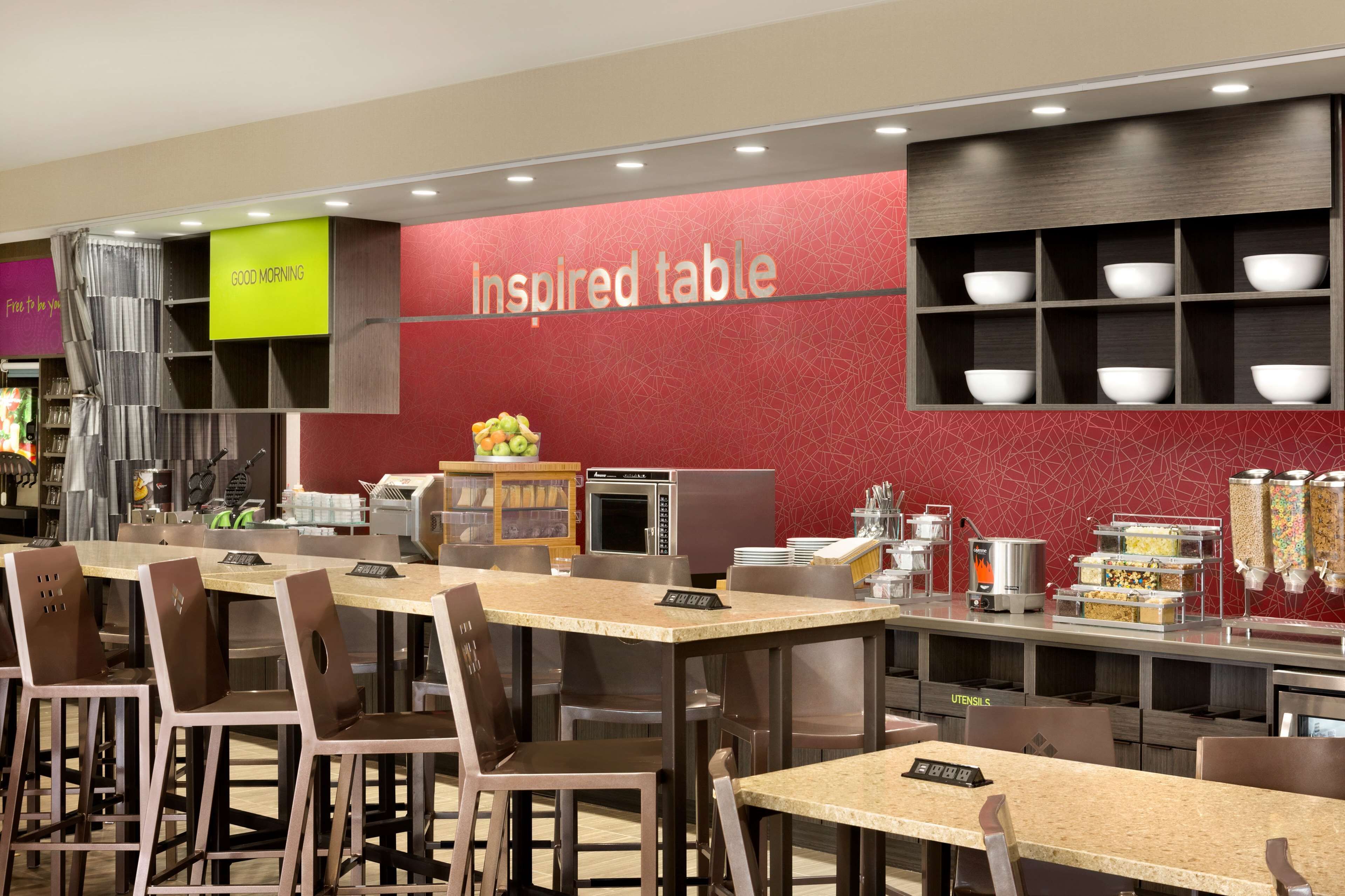 A modern restaurant with a red wall labeled "Inspired table," a buffet area with various food containers, and a seating area with tables and chairs.
