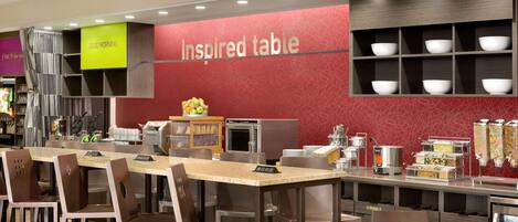 A modern restaurant with a red wall labeled "Inspired table," a buffet area with various food containers, and a seating area with tables and chairs.