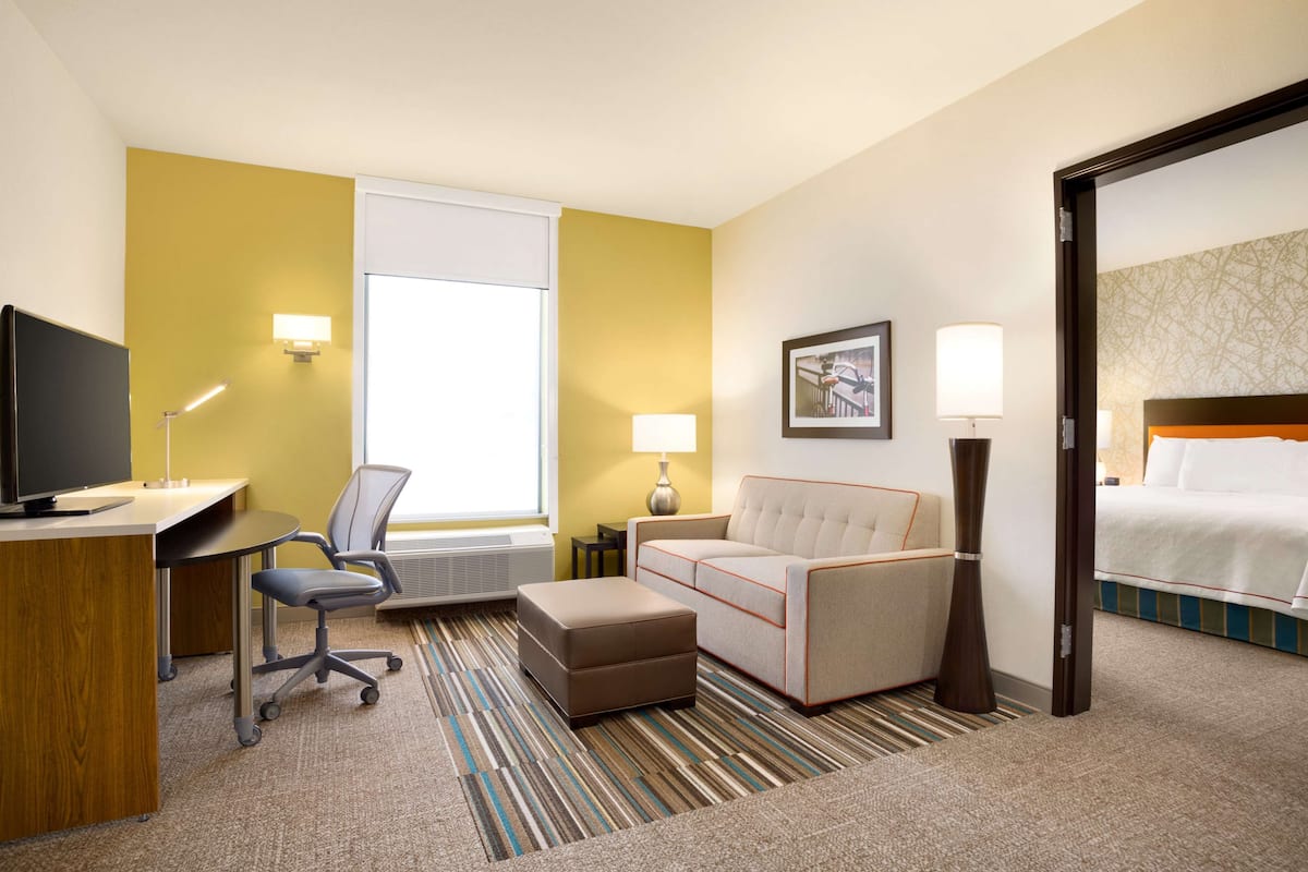 A hotel room with a desk, chair, ottoman, sofa, and a bed.