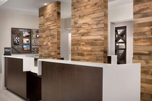A reception desk with a modern design, featuring a wooden wall panel and a framed collage of cityscape photos. - Hilton Garden Inn Downtown Birmingham (Birmingham)