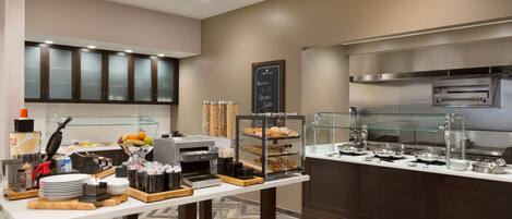 Montaje de bufé con diferentes alimentos, una estación de café y un horno para pizzas.