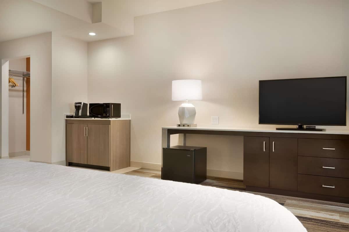 Hotellihuone, jossa on sänky, työpöytä lampun kanssa, televisio ja minibaari.