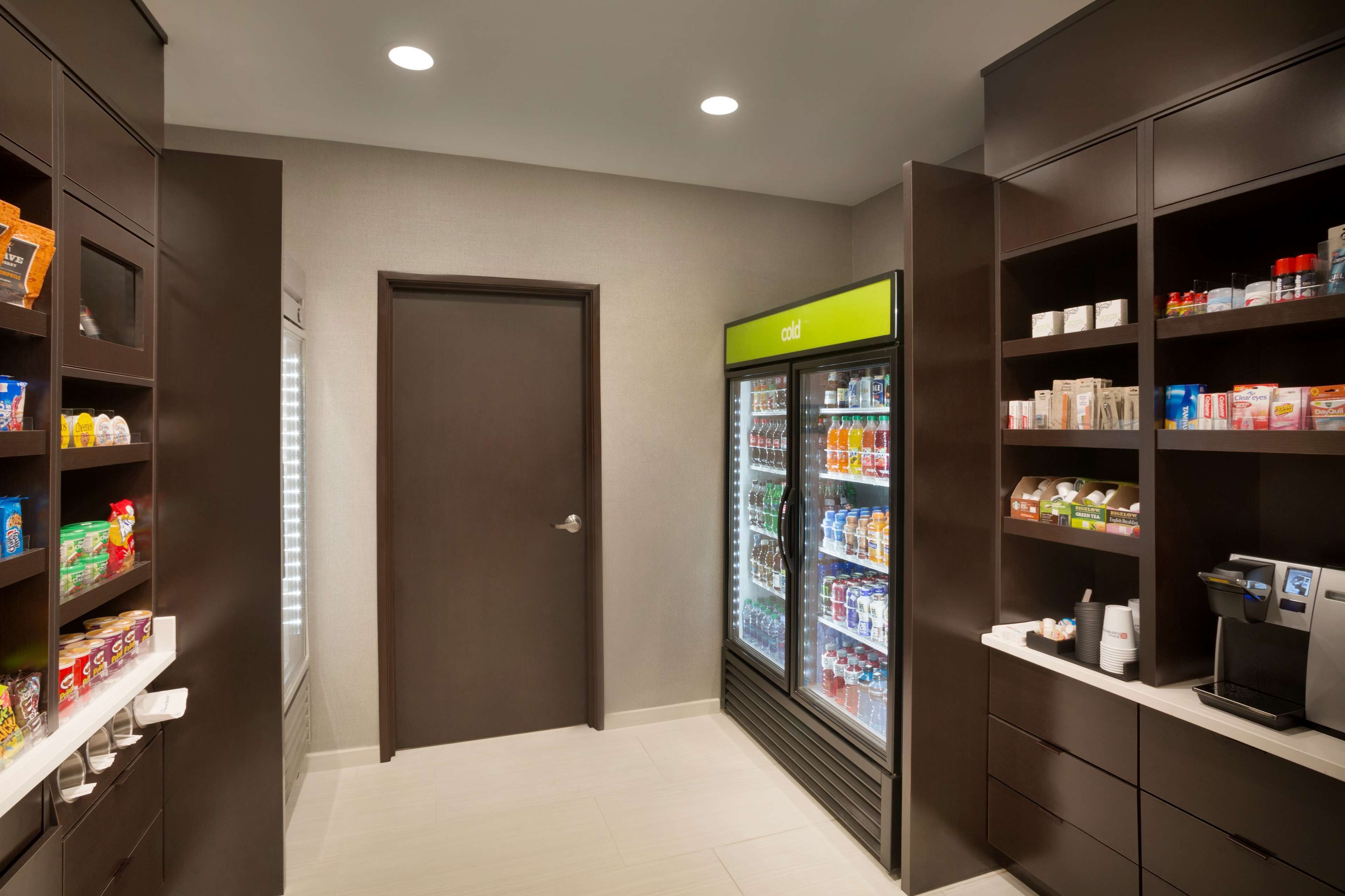 Una despensa de hotel con estantes llenos de refrigerios, un refrigerador con bebidas y una máquina de café.