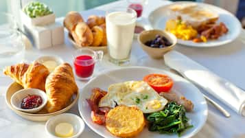 Mesa de café da manhã com croissants, ovos, bacon, torradas e diversas geleias.