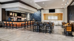 Uma área de bar moderna com balcão, banquetas e um espaço de estar com mesas e cadeiras.