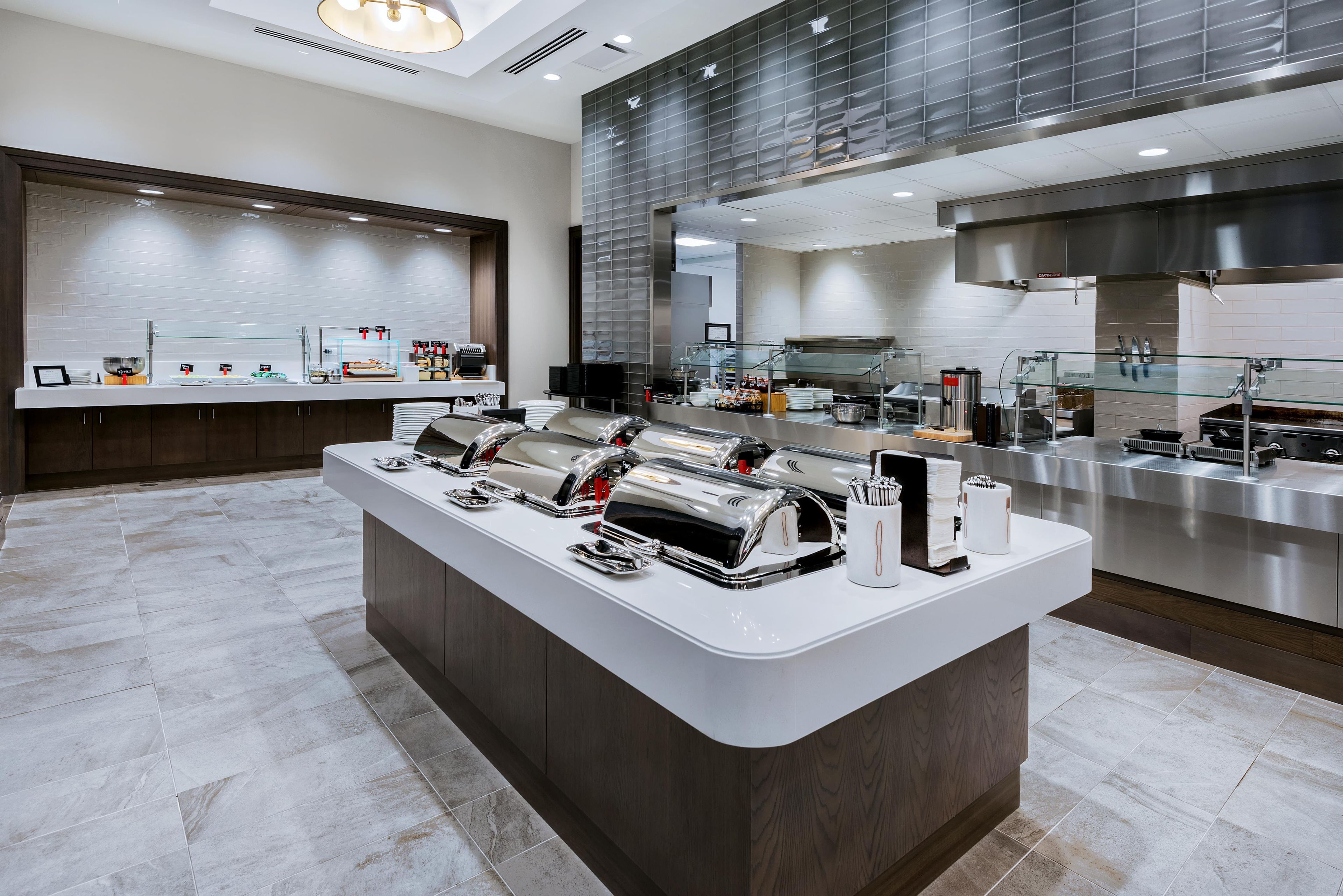 A modern kitchen with stainless steel appliances, a central island with utensils, and a buffet area with food items.