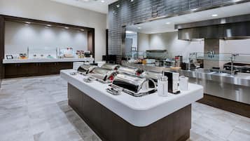 A modern kitchen with stainless steel appliances, a central island with utensils, and a buffet area with food items.