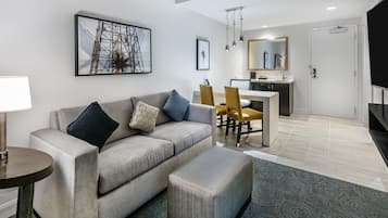 A modern living room with a sofa, ottoman, and a dining area with chairs.