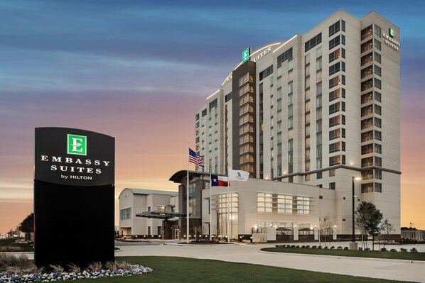 A hotel building with a sign for Embassy Suites by Hilton, featuring a modern design with multiple floors and a flagpole with flags.