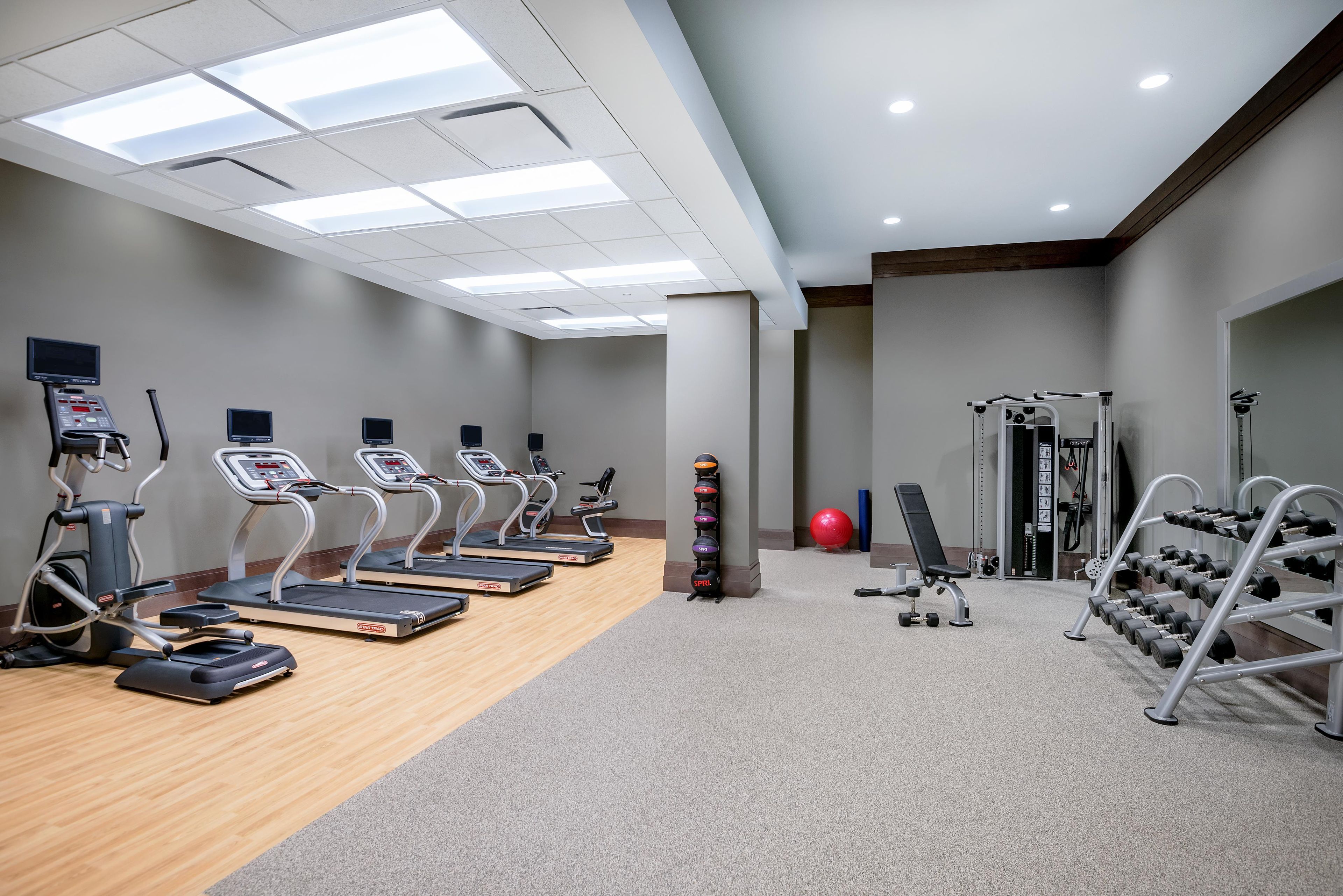 A gym with treadmills, weight machines, and a red exercise ball.