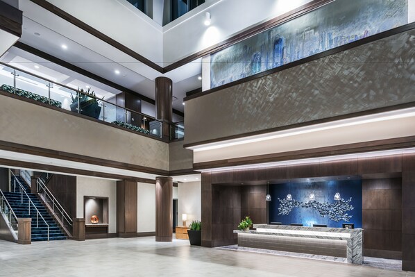 A spacious lobby with a reception desk, a staircase, and a large cityscape mural.