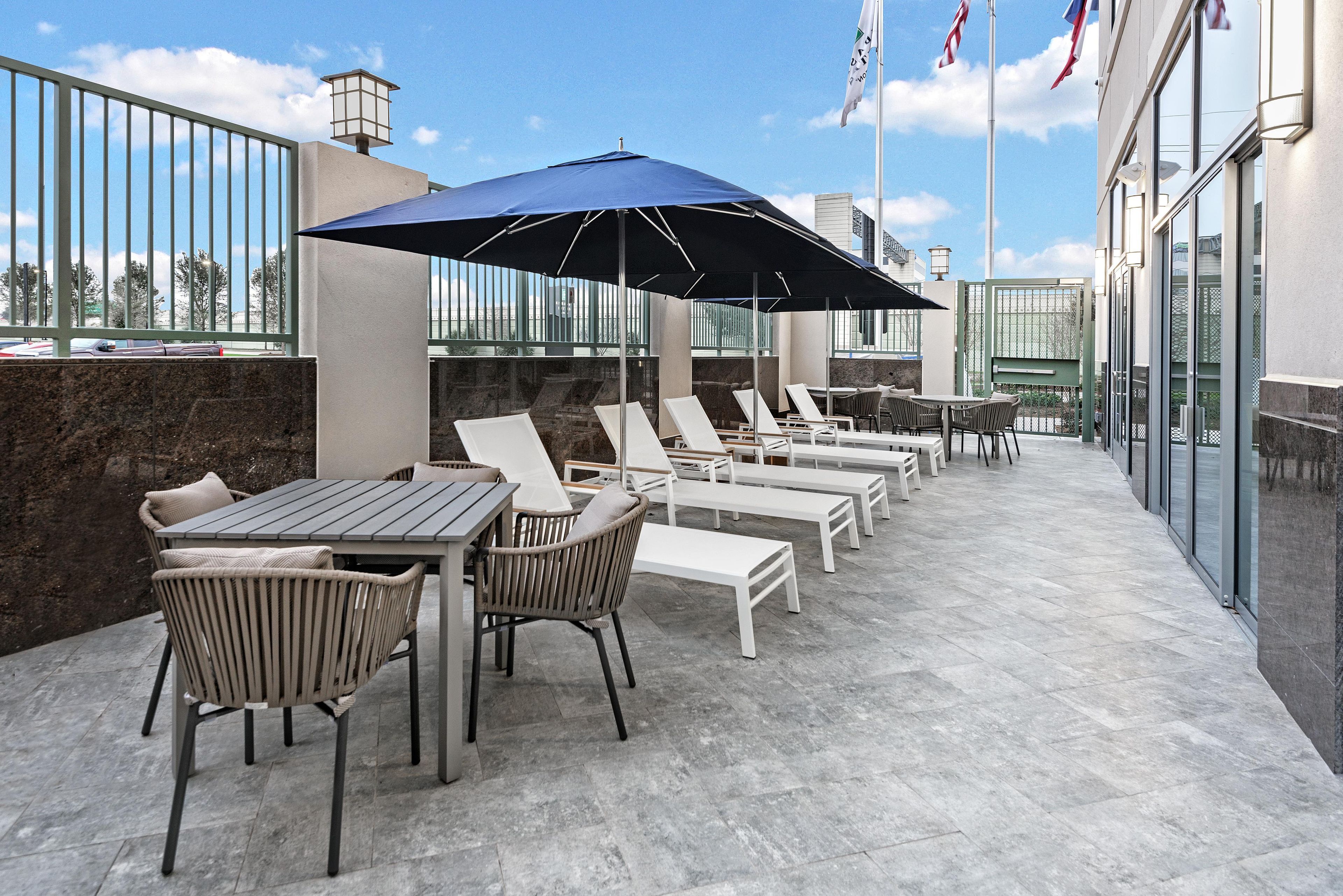 An outdoor patio with tables and chairs, a large umbrella, and a view of the cityscape.