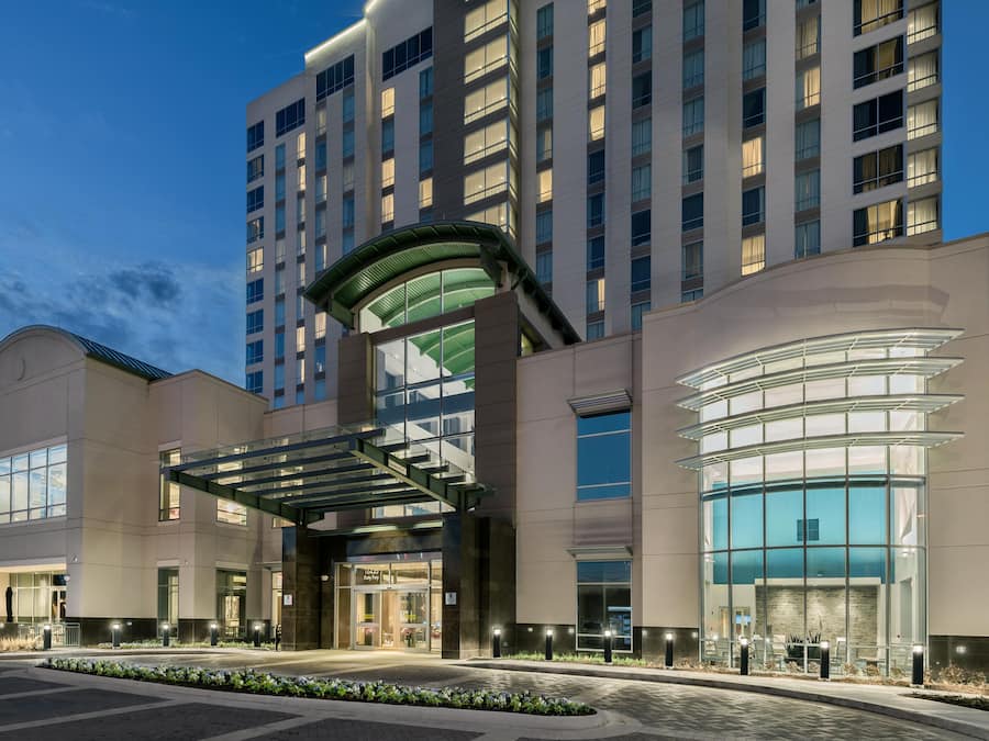 A modern hotel with a glass facade, a covered entrance, and a landscaped entrance area.