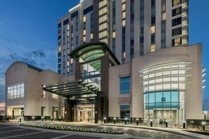 A modern hotel with a glass facade, a covered entrance, and a landscaped entrance area.