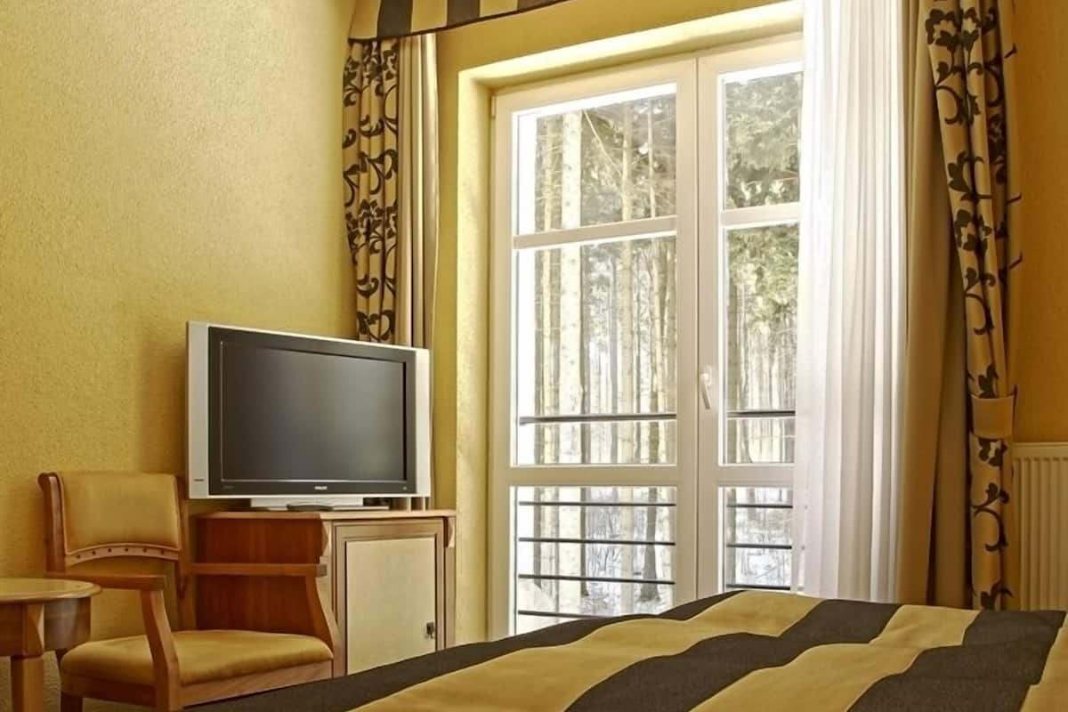 Ein Hotelzimmer mit einem Bett, einem Fernseher auf einem Tisch, einem Sessel und einem Fenster mit Vorhängen.