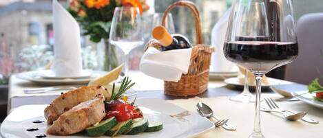 A dining table with a plate of grilled chicken and vegetables, a basket of bread, and a glass of red wine.