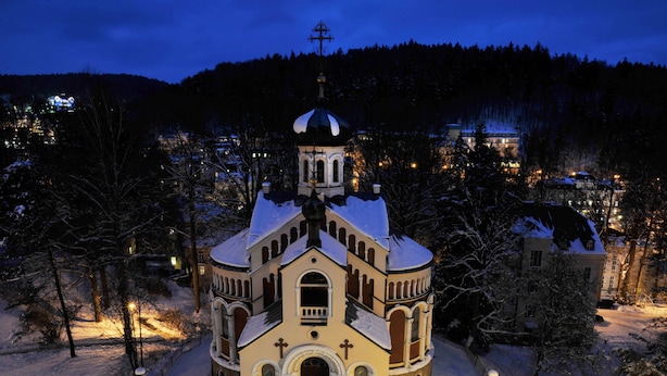 A snow-covered church with a bell tower, surrounded by trees and a snowy landscape.