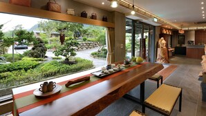 A modern interior with a long wooden table, a view of a garden, and a statue. - Country Road B&B (Toucheng)